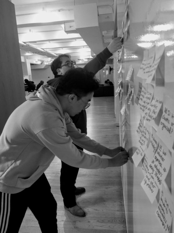 Black and white photo of 2 men doing affinity mapping by placing post-it notes to whiteboard